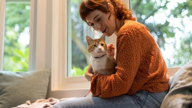Frau in orangem Pullover hält ihre Katze am Arm